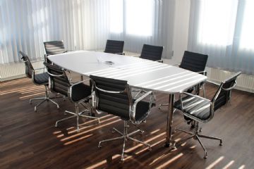 L'immagine rappresenta un ufficio con un tavolo di lavoro attorniato da 8 sedie vuote